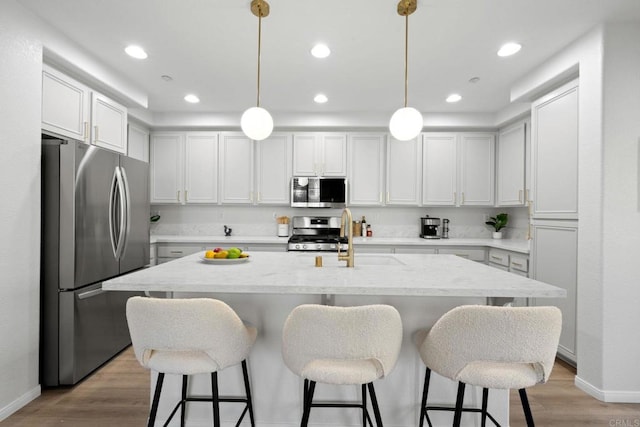 kitchen with appliances with stainless steel finishes, an island with sink, light hardwood / wood-style floors, and pendant lighting