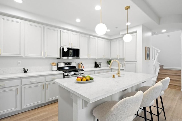 kitchen with decorative light fixtures, light hardwood / wood-style floors, sink, a kitchen island with sink, and appliances with stainless steel finishes