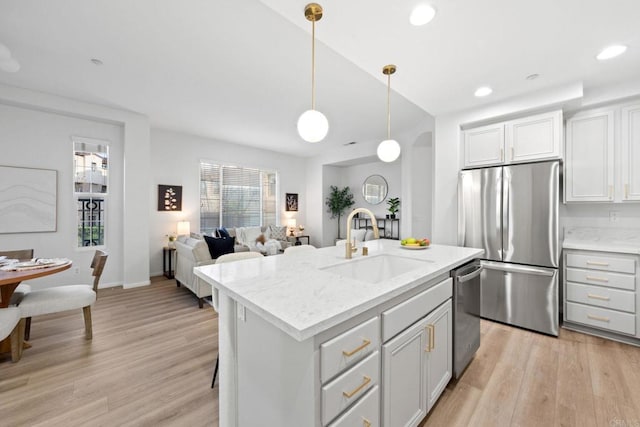 kitchen with an island with sink, appliances with stainless steel finishes, decorative light fixtures, light stone countertops, and sink