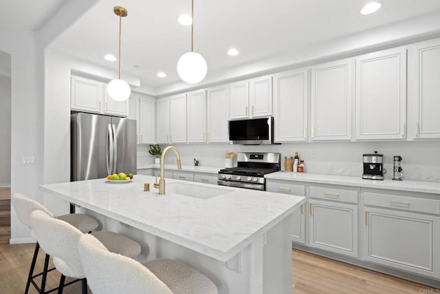 kitchen with a center island with sink, appliances with stainless steel finishes, pendant lighting, white cabinets, and sink