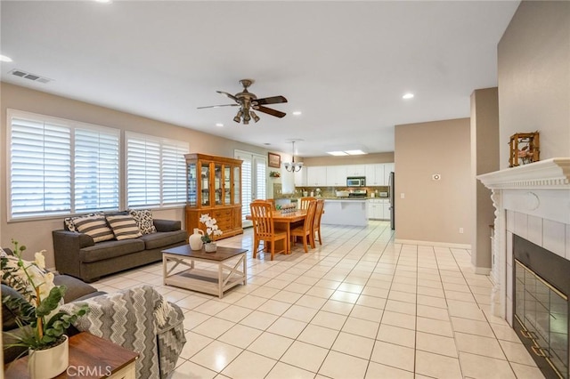 living room with ceiling fan, light tile patterned floors, a tiled fireplace, and a healthy amount of sunlight