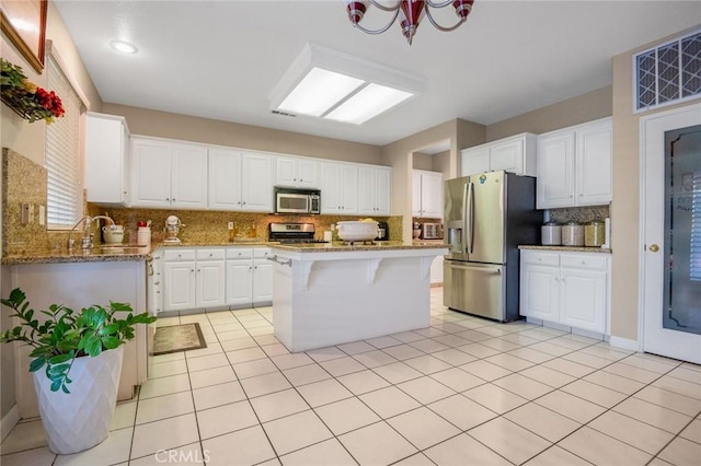 kitchen featuring light stone countertops, appliances with stainless steel finishes, white cabinetry, backsplash, and a breakfast bar area