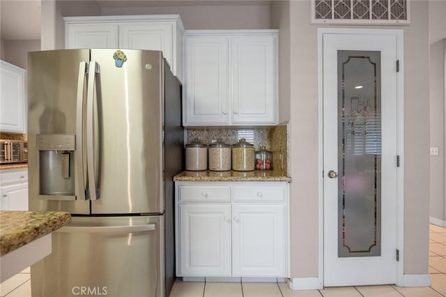 kitchen featuring light stone countertops, light tile patterned floors, stainless steel fridge, and white cabinetry