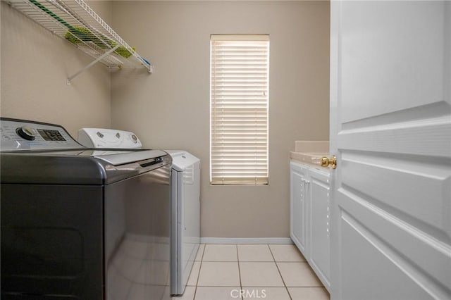 clothes washing area featuring cabinets, light tile patterned flooring, and washing machine and clothes dryer