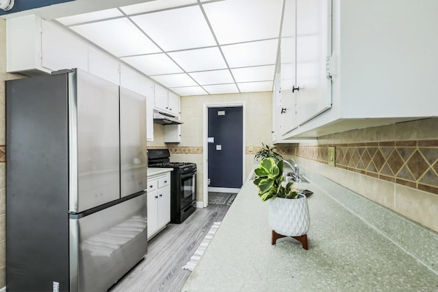 kitchen with black gas range, stainless steel refrigerator, light wood-type flooring, a paneled ceiling, and white cabinets