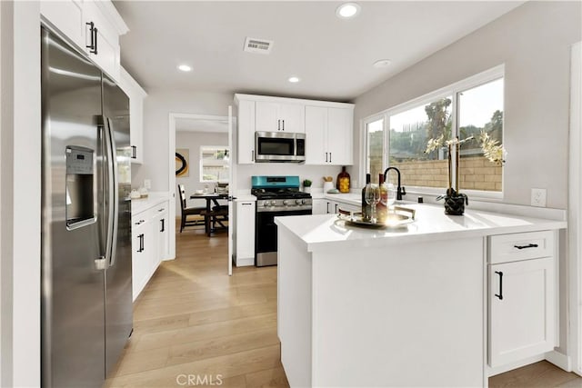 kitchen with light hardwood / wood-style floors, kitchen peninsula, white cabinets, and stainless steel appliances