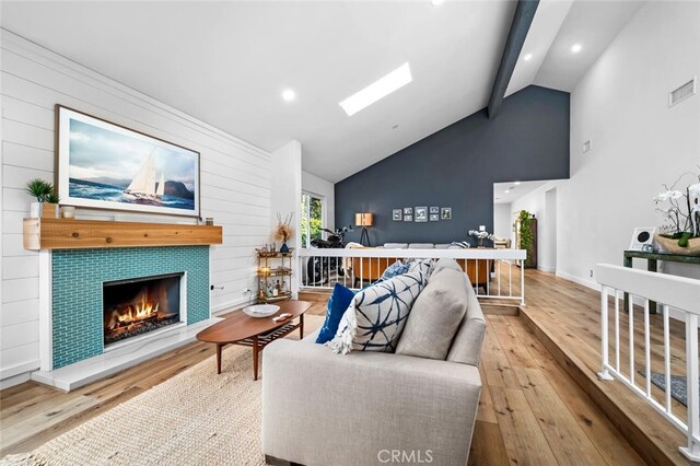 living room with hardwood / wood-style flooring, a fireplace, lofted ceiling with skylight, and wooden walls