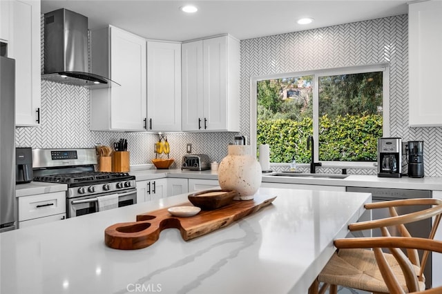 kitchen featuring stainless steel gas stove, white cabinets, sink, and wall chimney exhaust hood