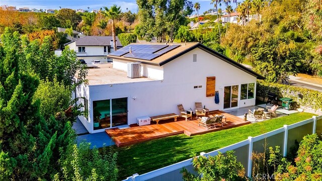 rear view of property featuring a wooden deck, a yard, and solar panels