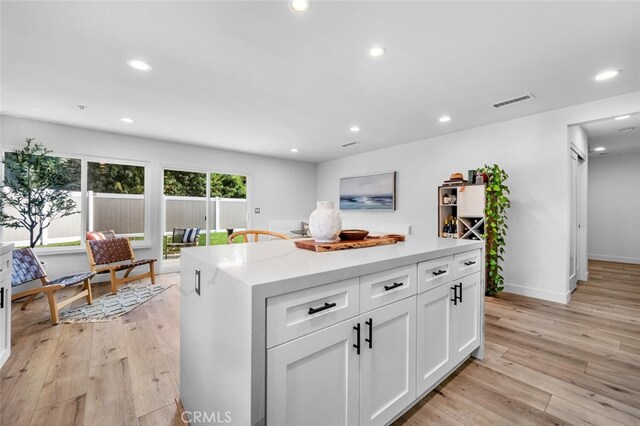 kitchen featuring light hardwood / wood-style floors, light stone counters, white cabinetry, and a center island