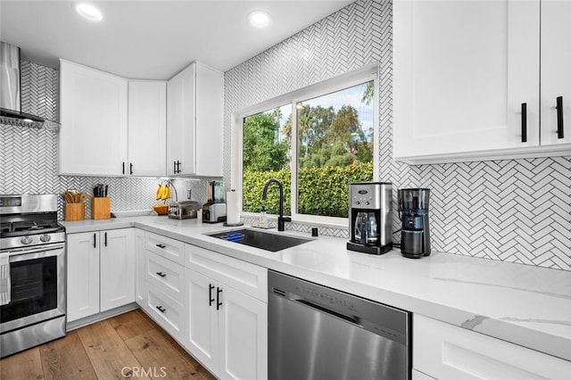 kitchen with sink, white cabinetry, light wood-type flooring, appliances with stainless steel finishes, and wall chimney range hood