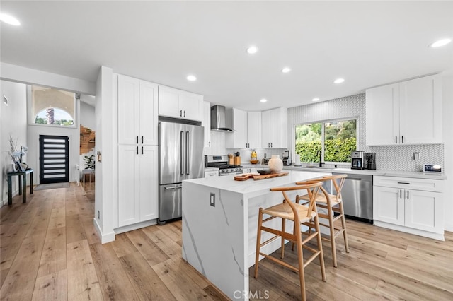 kitchen with white cabinetry, appliances with stainless steel finishes, wall chimney exhaust hood, and a kitchen island