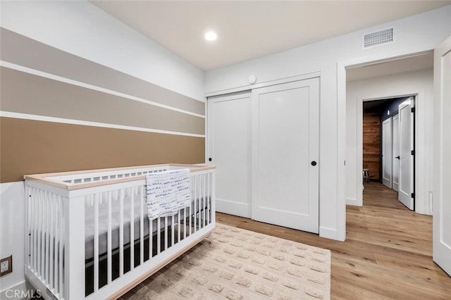 unfurnished bedroom featuring a crib, light wood-type flooring, and a closet