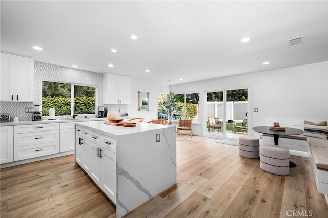 kitchen featuring sink, backsplash, white cabinets, a center island, and light wood-type flooring