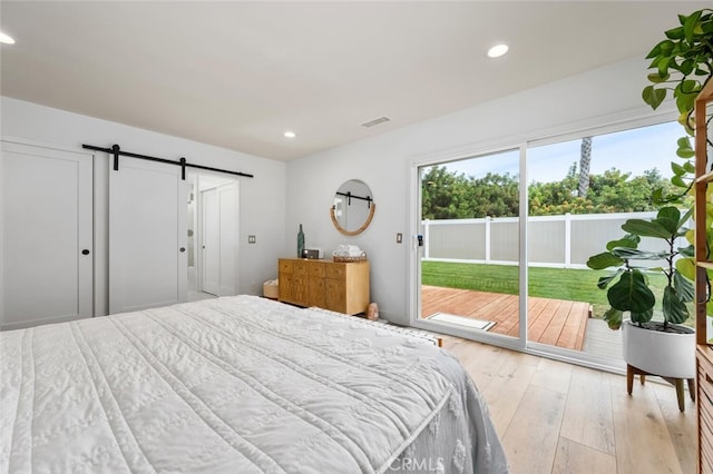 bedroom featuring a barn door, light hardwood / wood-style floors, and access to exterior