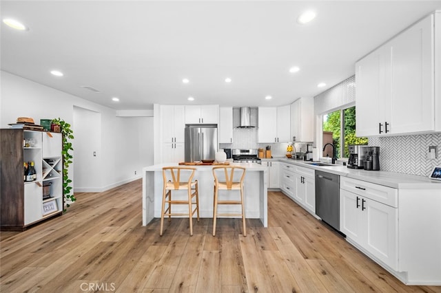 kitchen featuring white cabinetry, wall chimney exhaust hood, stainless steel appliances, and a kitchen island