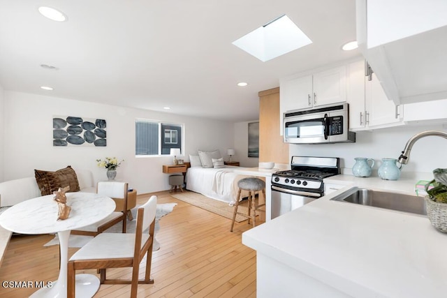 kitchen featuring sink, a skylight, stainless steel appliances, white cabinets, and light wood-type flooring