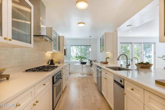 kitchen with wall chimney exhaust hood, sink, white cabinetry, pendant lighting, and stainless steel appliances