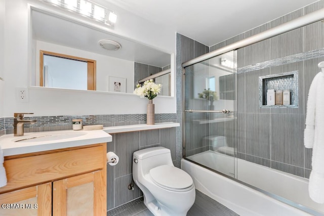 full bathroom with tile walls, decorative backsplash, enclosed tub / shower combo, vanity, and toilet