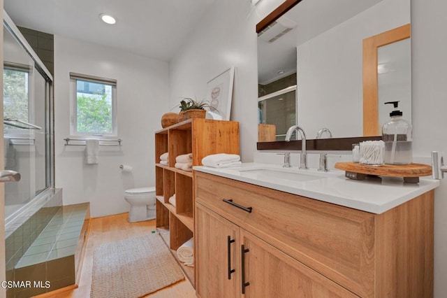 bathroom with wood-type flooring, a shower with shower door, vanity, and toilet