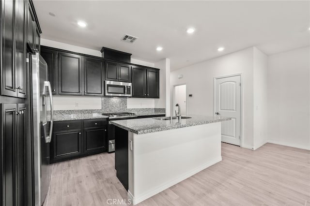 kitchen featuring light hardwood / wood-style floors, an island with sink, stainless steel appliances, light stone counters, and sink