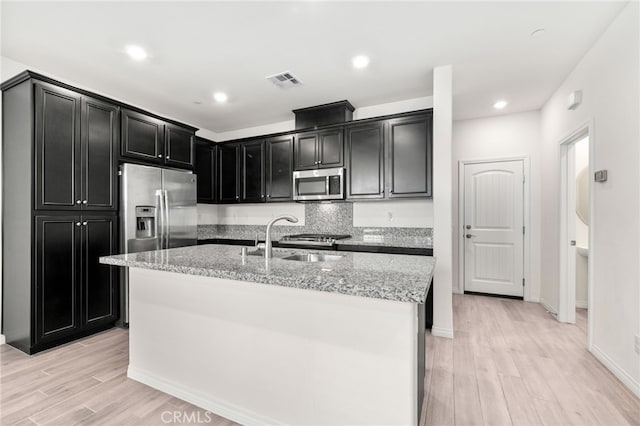 kitchen featuring light stone countertops, stainless steel appliances, sink, a kitchen island with sink, and light wood-type flooring