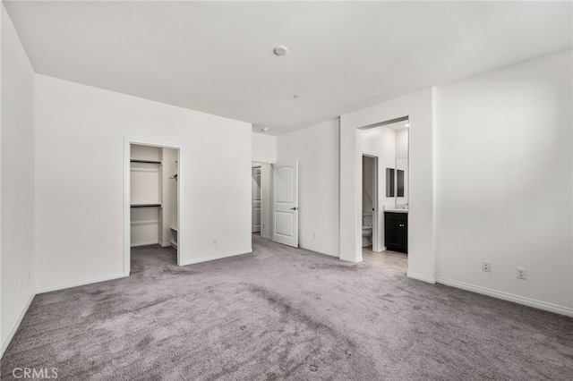 unfurnished bedroom featuring a spacious closet, ensuite bathroom, a closet, and carpet floors