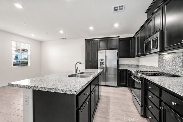 kitchen with appliances with stainless steel finishes, sink, light hardwood / wood-style floors, and a center island with sink