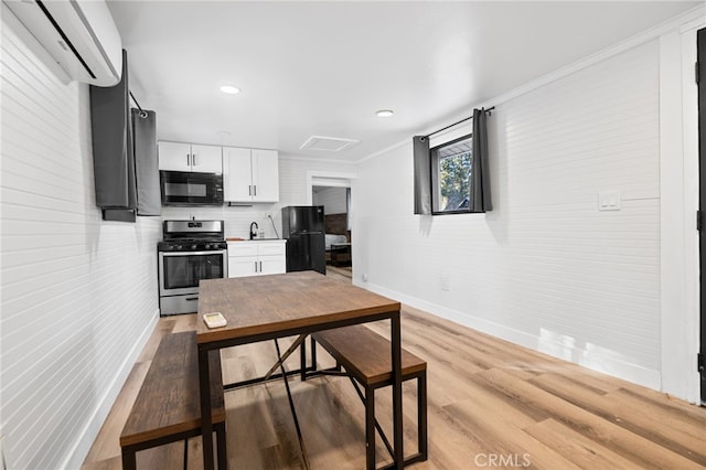 kitchen with black appliances, white cabinetry, ornamental molding, a wall unit AC, and light hardwood / wood-style flooring