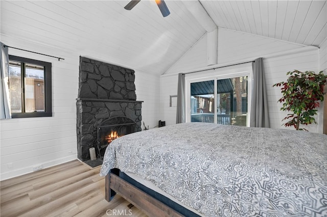 bedroom with a stone fireplace, vaulted ceiling with beams, access to exterior, hardwood / wood-style flooring, and ceiling fan