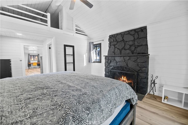 bedroom featuring a fireplace, wooden walls, hardwood / wood-style flooring, high vaulted ceiling, and ceiling fan