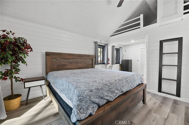 bedroom featuring hardwood / wood-style flooring, ceiling fan, wood walls, and high vaulted ceiling