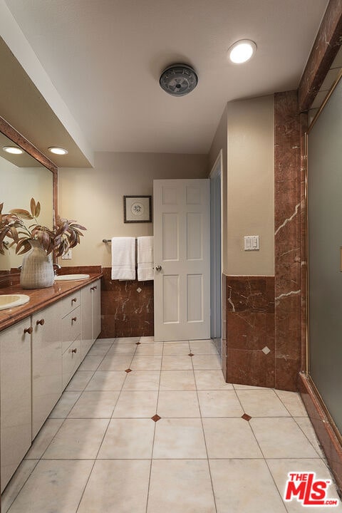 bathroom featuring tile patterned flooring, vanity, tile walls, and a shower with door