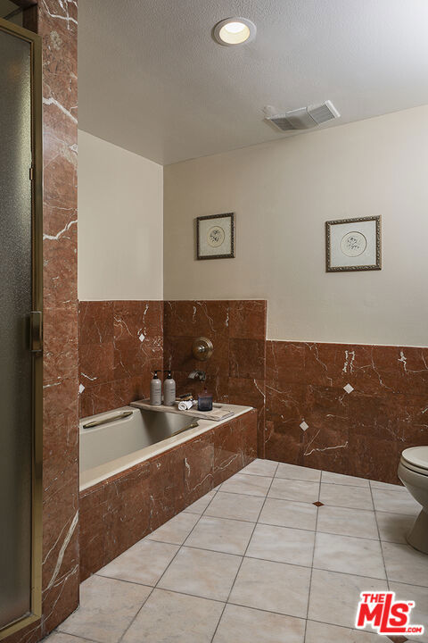 bathroom with tiled bath, tile walls, toilet, and a textured ceiling