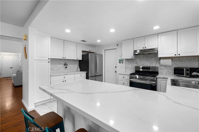 kitchen with sink, white cabinetry, light stone countertops, appliances with stainless steel finishes, and a breakfast bar area