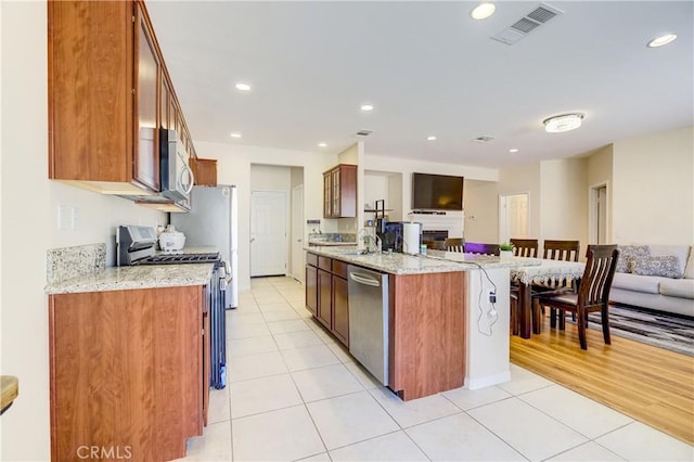 kitchen featuring light tile patterned floors, an island with sink, stainless steel appliances, light stone counters, and a breakfast bar