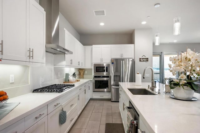 kitchen with pendant lighting, wall chimney exhaust hood, white cabinetry, stainless steel appliances, and sink