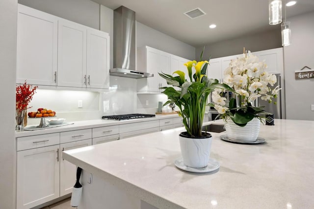 kitchen with hanging light fixtures, white cabinets, stainless steel gas stovetop, and wall chimney range hood