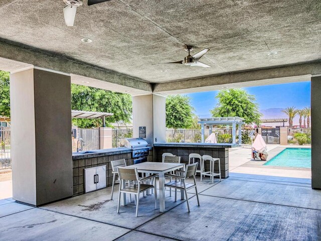 patio terrace at dusk with a grill, an outdoor kitchen, a fenced in pool, ceiling fan, and an outdoor wet bar