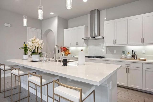 kitchen with a breakfast bar, pendant lighting, a center island with sink, and wall chimney exhaust hood