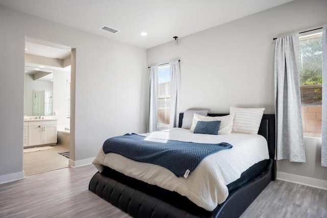 bedroom with sink, connected bathroom, and light hardwood / wood-style flooring