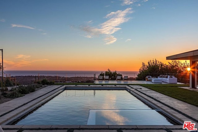 pool at dusk with an outdoor living space, a patio area, and a water view