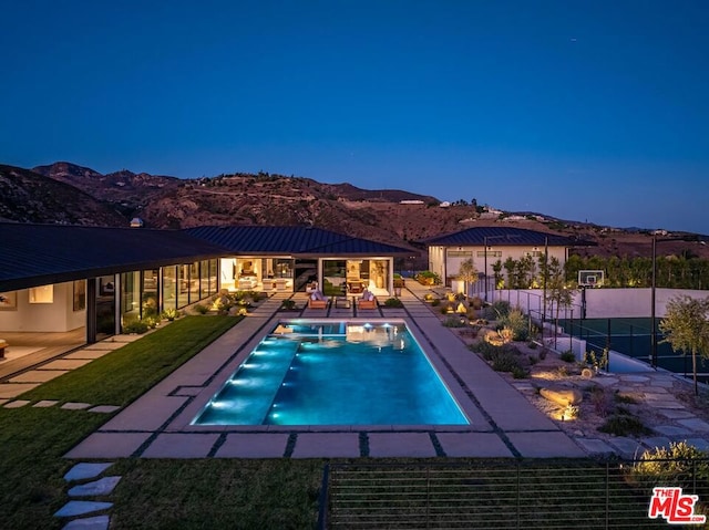 pool at dusk with a mountain view, a patio area, and a yard