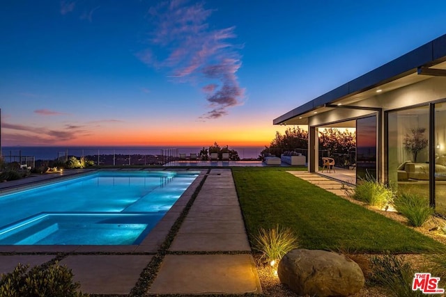 pool at dusk with a patio area, an in ground hot tub, and a lawn