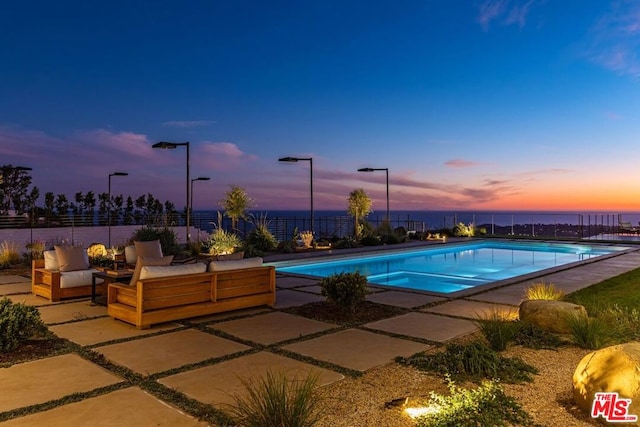 pool at dusk with an outdoor living space and a patio