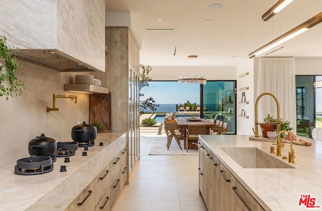 kitchen with light tile patterned floors, light brown cabinets, decorative light fixtures, a chandelier, and sink