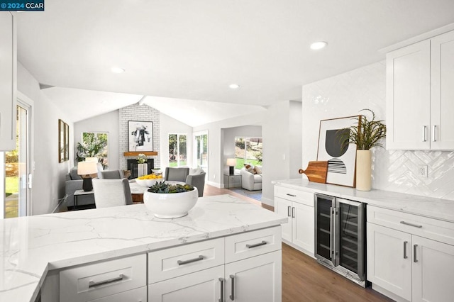 kitchen featuring tasteful backsplash, vaulted ceiling, white cabinetry, light stone countertops, and beverage cooler