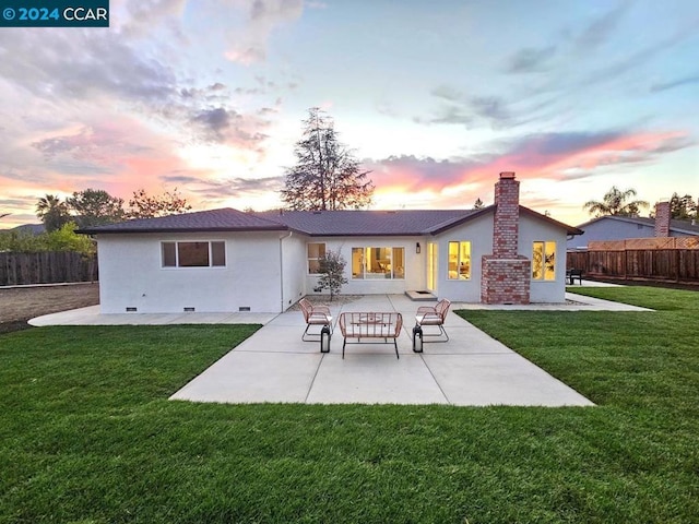 back house at dusk featuring a lawn and a patio