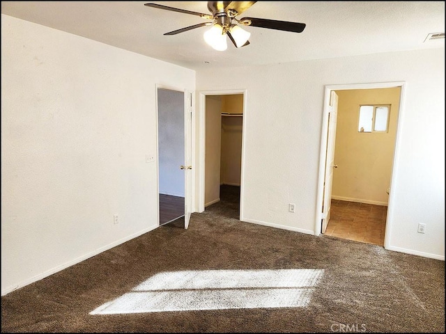 unfurnished bedroom with ceiling fan, ensuite bath, a walk in closet, a closet, and dark carpet