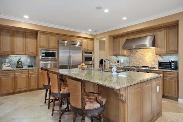 kitchen with sink, built in appliances, light stone counters, a kitchen island with sink, and crown molding